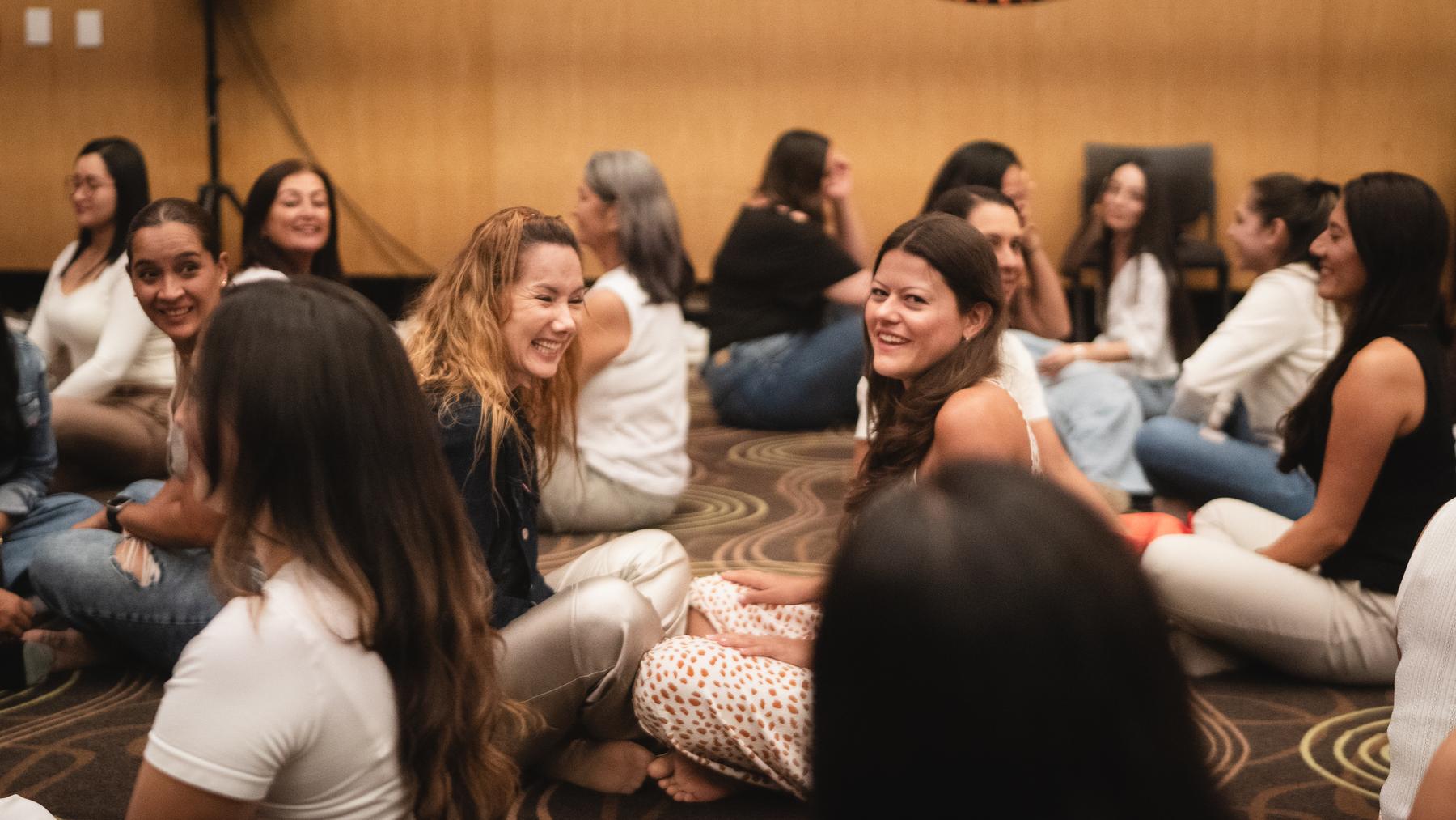 Un grupo de mujeres sentadas en el suelo conversa y ríe durante un ejercicio en Vibra Fest