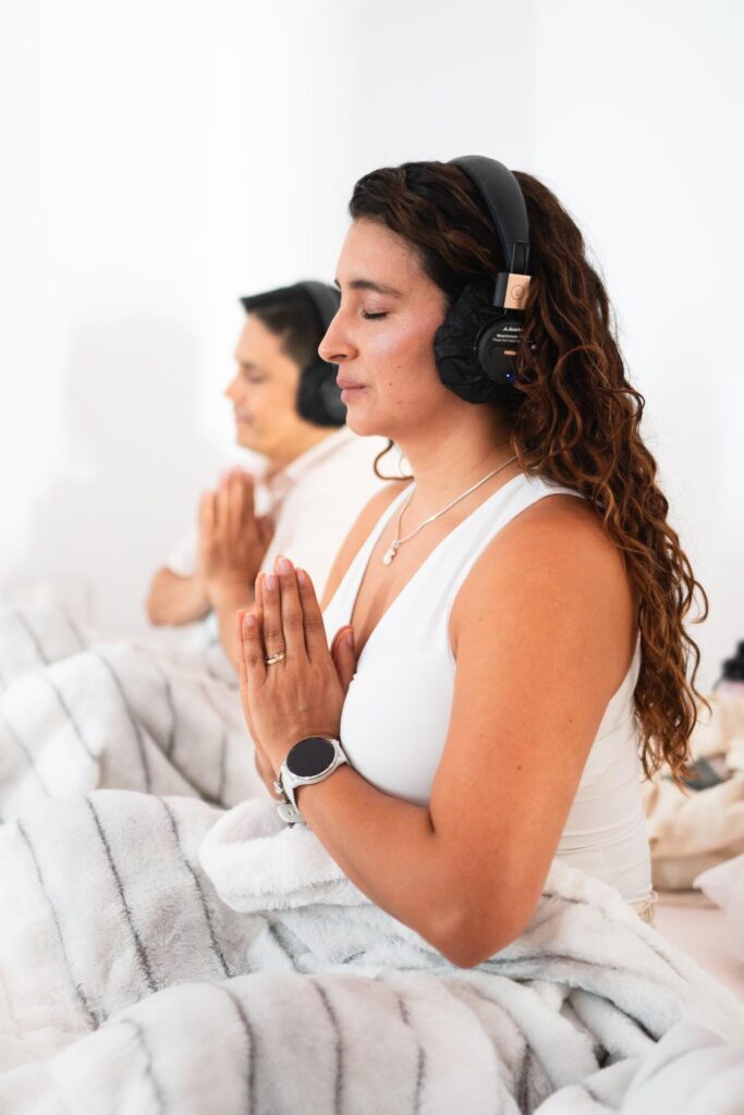 Mujer meditando con audífonos y las manos juntas frente al pecho